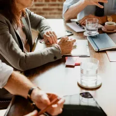 Close-up of hands and notebooks during a business meeting at a table with drinks and stationery.