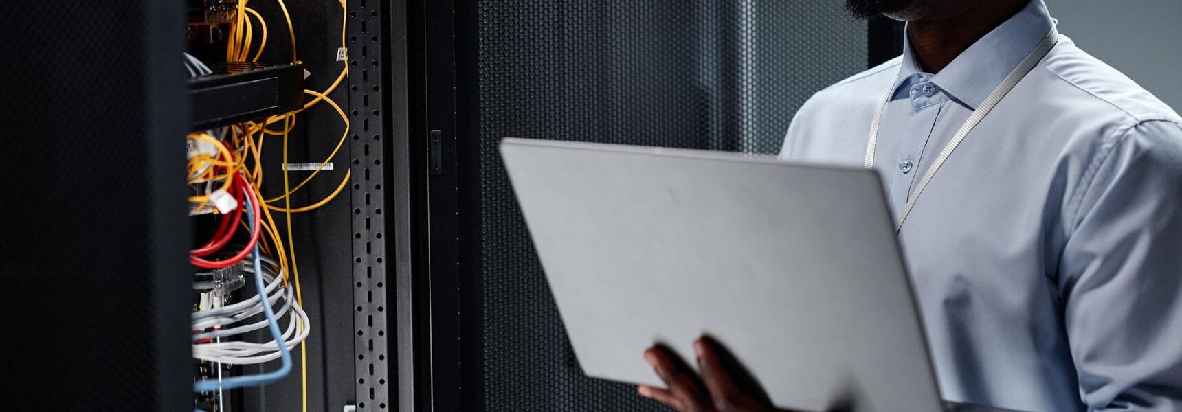 Individual holding a laptop while examining server equipment in a data center.