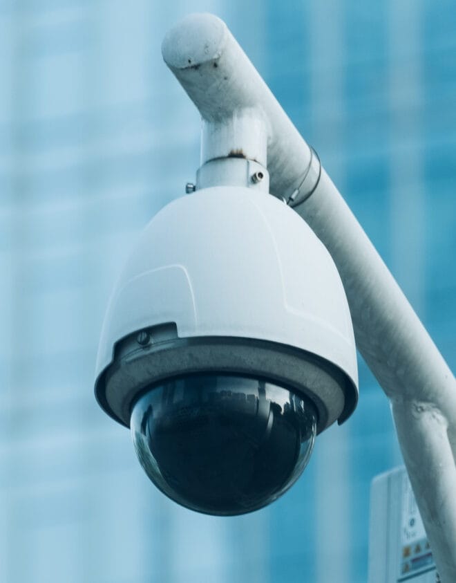 White dome security camera mounted on a pole with a blurred background.