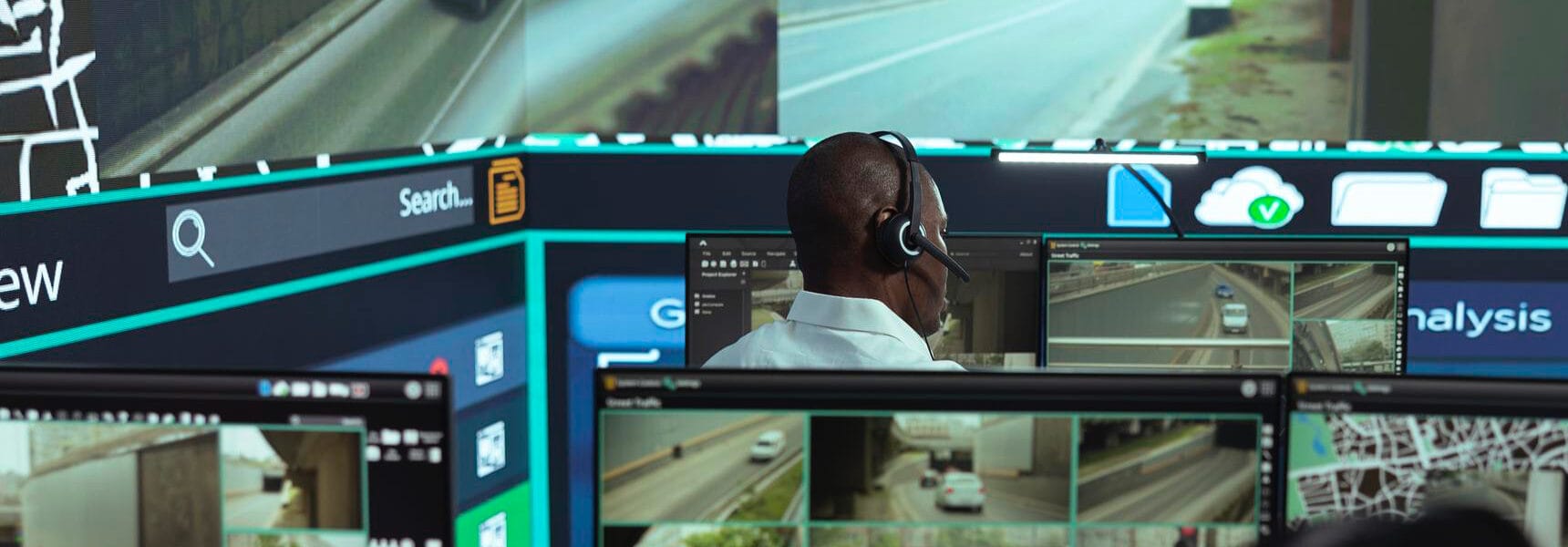 Individual wearing a headset monitoring traffic through multiple computer screens displaying video feeds.