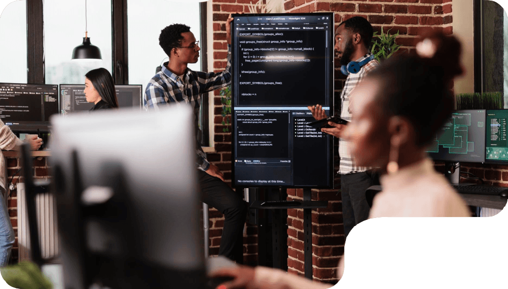A group of individuals discussing a coding project in a modern workspace with computer screens and a large display.